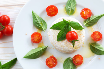 round piece of cheese with basil and cherry tomatoes on a white plate