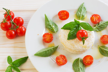 round piece of cheese with basil and cherry tomatoes on a white plate