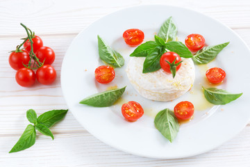round piece of cheese with basil and cherry tomatoes on a white plate