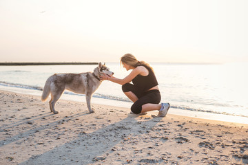 young caucasian female playing with siberian husky dog on beach during sunrise