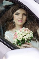 Portrait of a girl behind wet glass. The bride in a wedding car.