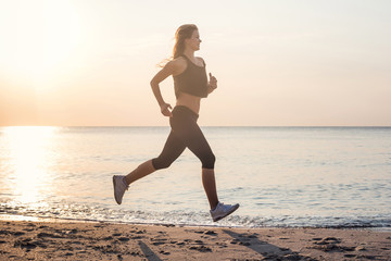 Fototapeta na wymiar Running woman. Female runner jogging during the sunrise on beach.