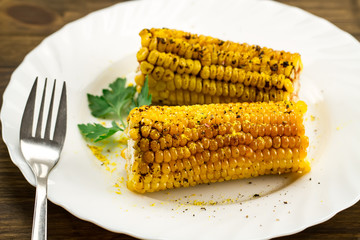 roasted corn on a white plate with spices on wooden background. Healthy vegetarian food.