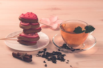 delicious fresh cookies in the shape of a heart on a white plate on wooden background. Cup of green tea. Breakfast