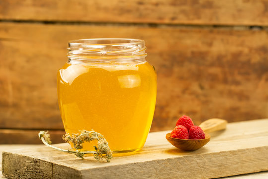 glass jar of honey with drizzler, raspberries, dried flowers on wooden background