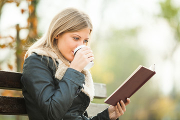 Young woman reading book and drinking coffee to go