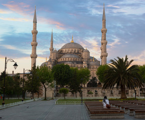 Fototapeta na wymiar girl sitting on a bench looks at the Blue mosque lit with a sunrise