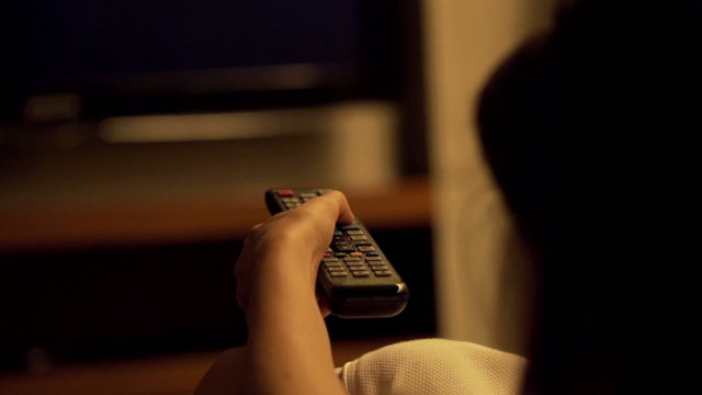 Woman watching TV at night and changing channels with remote
