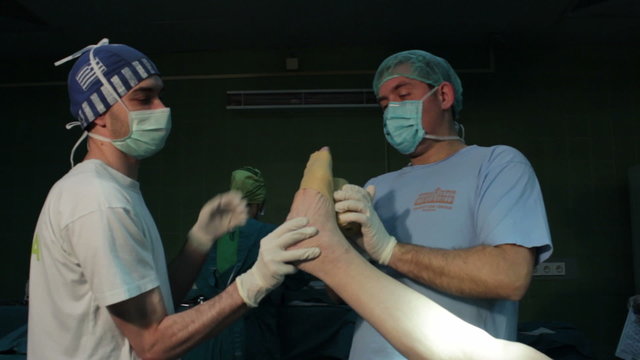 Two male paramedic bandaging and isolated leg of patient for surgical operation in operating room,close up.medic wearing protective gloves  and masks.