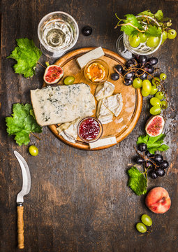 Gorgonzola Camembert on a wooden cutting board with a knife for cheese with honey and jam light grape on dark wooden background close up