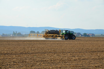 Fototapeta premium Plowed field with a tractor treating the soil