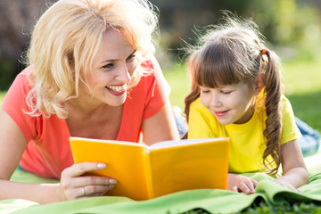 Mother and daughter reading a book at the park.