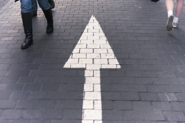 Arrow straight on pavement walking street with walking people we