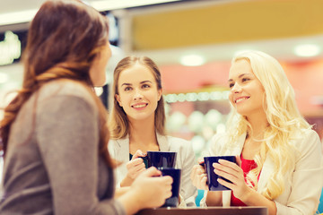 smiling young women with cups in mall or cafe