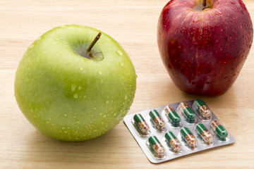 Green transparent capsules blister pack and fresh apples