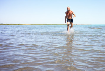 A strong man, athletic, running fast on the lake with a naked torso