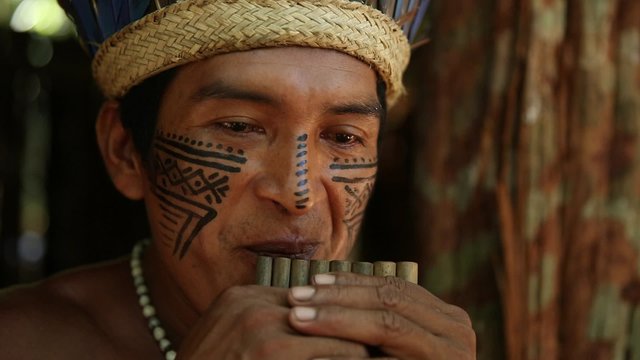 Native Brazilian playing wooden flute at an indigenous tribe in the Amazon