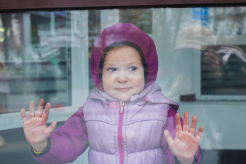 Portrait of toddler girl in warm hoodie through glass of display