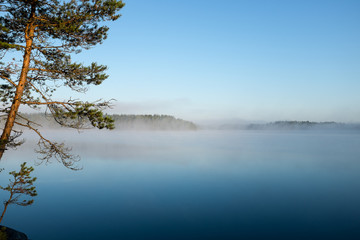 Beautiful lake view in early morning light and mist on lake surface, Finland.