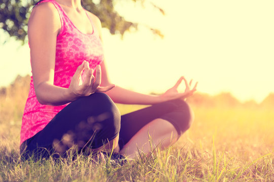Young athletic woman practicing yoga on a meadow at sunset, image with lens flare