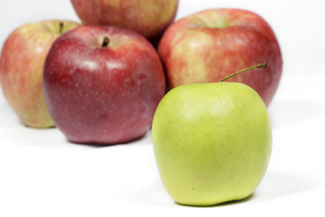 Green apple in front of several red apples