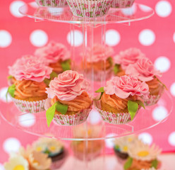 Delicious cupcakes with cream roses on the glass plate / Sweet buffet with cupcakes for a party, event or wedding in pink colors with dots 