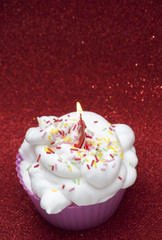 Cupcake with a lit candle over bright red background