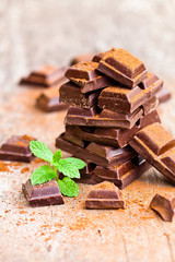 Pile of chocolate slices with mint on an old wooden table.