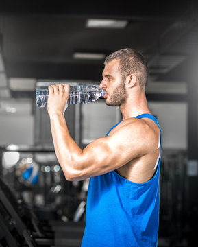 Young man drinking water in gym