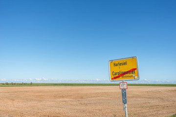 Ortsausgangsschild von Carolinensiel vor Kornfeld und dem Deich zur Nordsee
