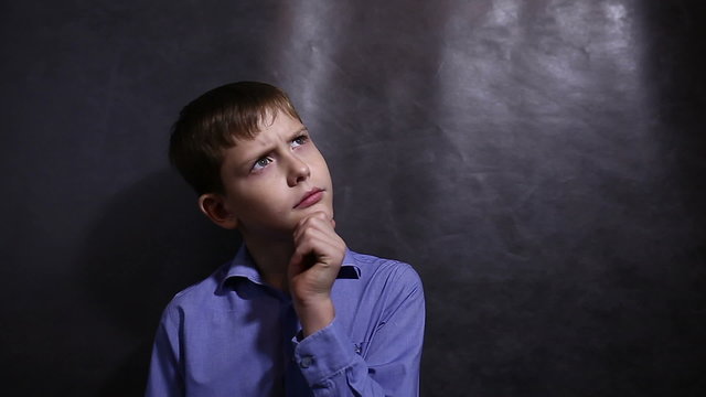 Teenage boy in a blue shirt is thinking looking away scratching