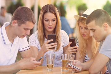 Four teenagers sitting in a cafe using their mobile phones