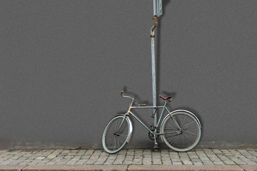 Old fashioned bicycle attached with lock to pole with road sign and gray wall in background