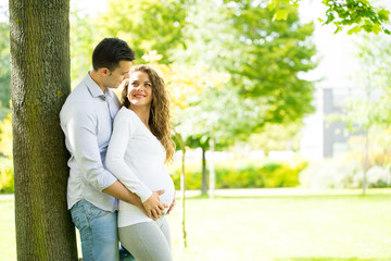 Naklejka premium Happy and young pregnant couple in park in summer