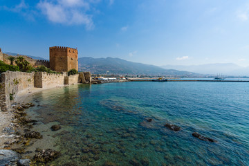 Fototapeta na wymiar Red Tower (Kizil Kule) and the ruins of the fortress wall near the shore. The Mediterranean coast. Alanya. Turkey