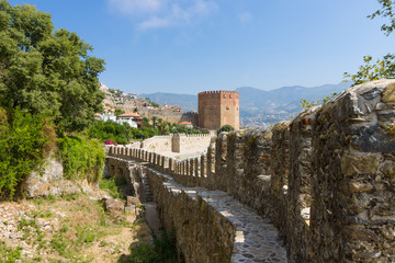 Fototapeta na wymiar Red Tower (Kizil Kule) and the ruins of the fortress wall. The Mediterranean coast. Alanya. Turkey