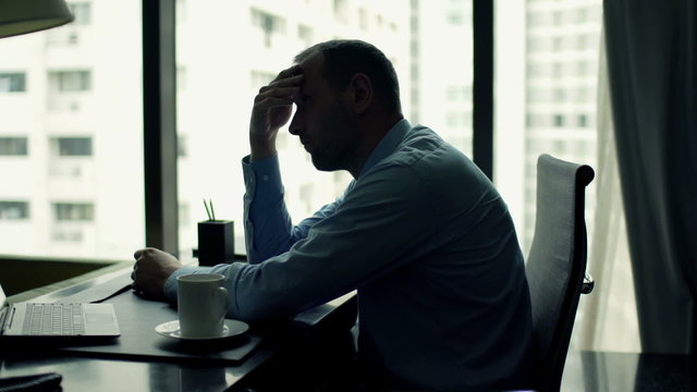 Sad, tired businessman sitting by desk in office
