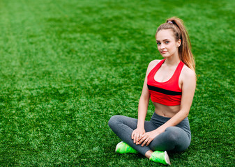 Young fitness girl sitting on green grass .
