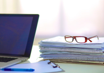 Laptop with stack of folders on table on white background