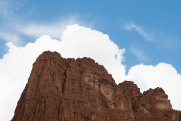 Red mountain surrounded by similar shaped clouds in front of a blue sky
