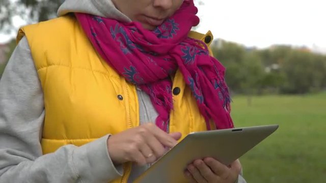 Woman In Yellow Vest Using Tablet Pc In The Park