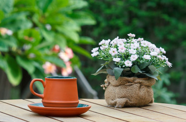 Cup of coffee and flowers with tree in background.