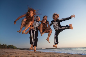 Group young girls in scary skeleton and wild savage costumes jumping high in air with fun before...