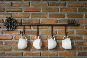 Coffee cups hanging on hooks in front of brick wall
