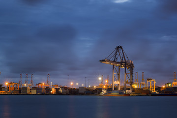 Container Cargo freight ship with working crane bridge in shipyard at dusk for Logistic Import Export background