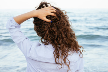 Young woman in shirt looking at the sea and keeps her hair