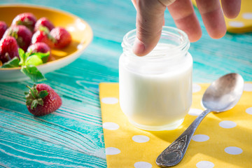 jar of yogurt and strawberry on turquoise colored wooden table