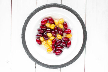 dogwood berries on white plate with on black tray on white colored wooden table. top view