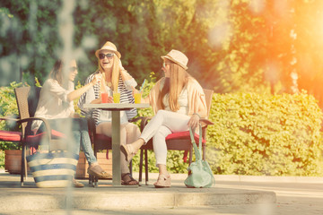 Three attractive girlfriends enjoying cocktails in an outdoor cafe, friendship concept
