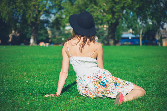 Young woman in hat sitting on grass in park